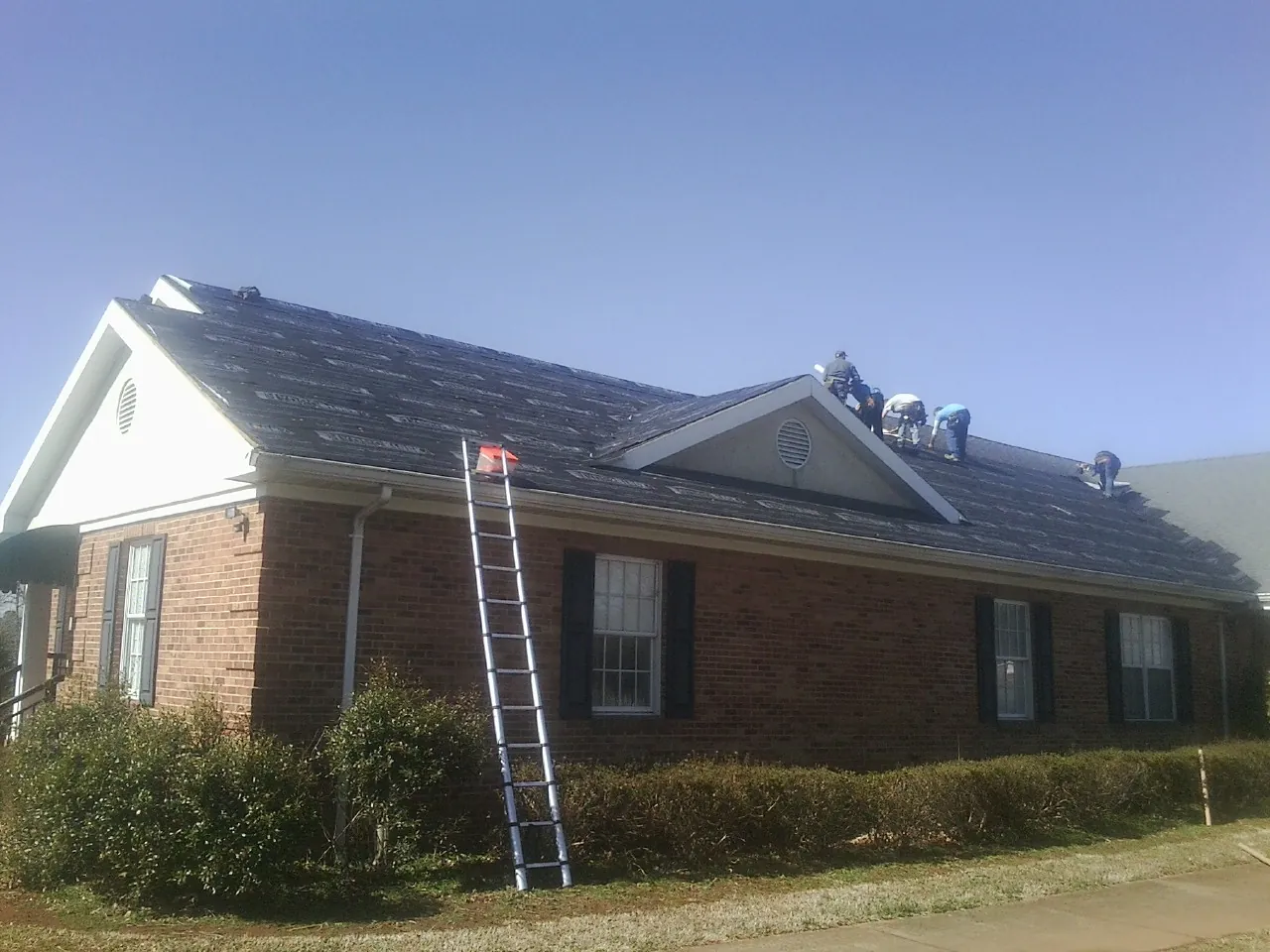 Crew tearing shingles off a brick ranch roof with a ladder set — Emergency Roof Repair work by our crew in Lomita
