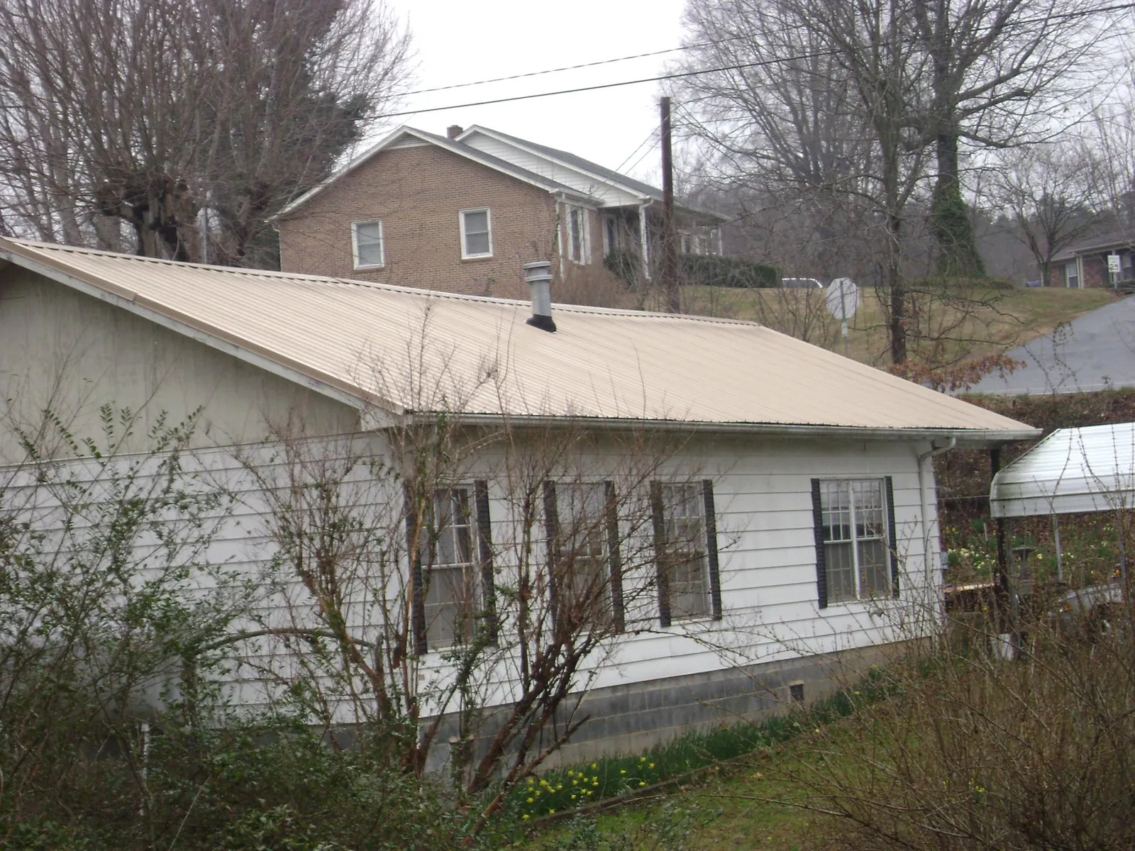Tan metal roof on a white sided house set into a hillside — Commercial Roofing by Roofing Brothers in Lomita